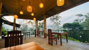 An outdoor seating area with tables and chairs, hanging lights, and a view of trees and hills. - 90 Degrees Ella (Ella)