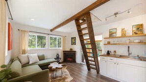 Ein modernes Wohnzimmer mit einem grünen Sofa, einer Holzlade, einem Kamin und einer Küche mit weißen Schränken und Regalen.