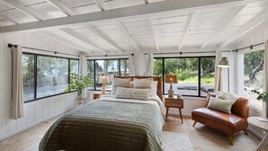 Ein geräumiges Schlafzimmer mit einem großen Bett, einem Ledersofa und mehreren Fenstern mit Blick ins Freie.