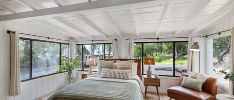A spacious bedroom with a large bed, a leather sofa, and multiple windows offering views of the outdoors.