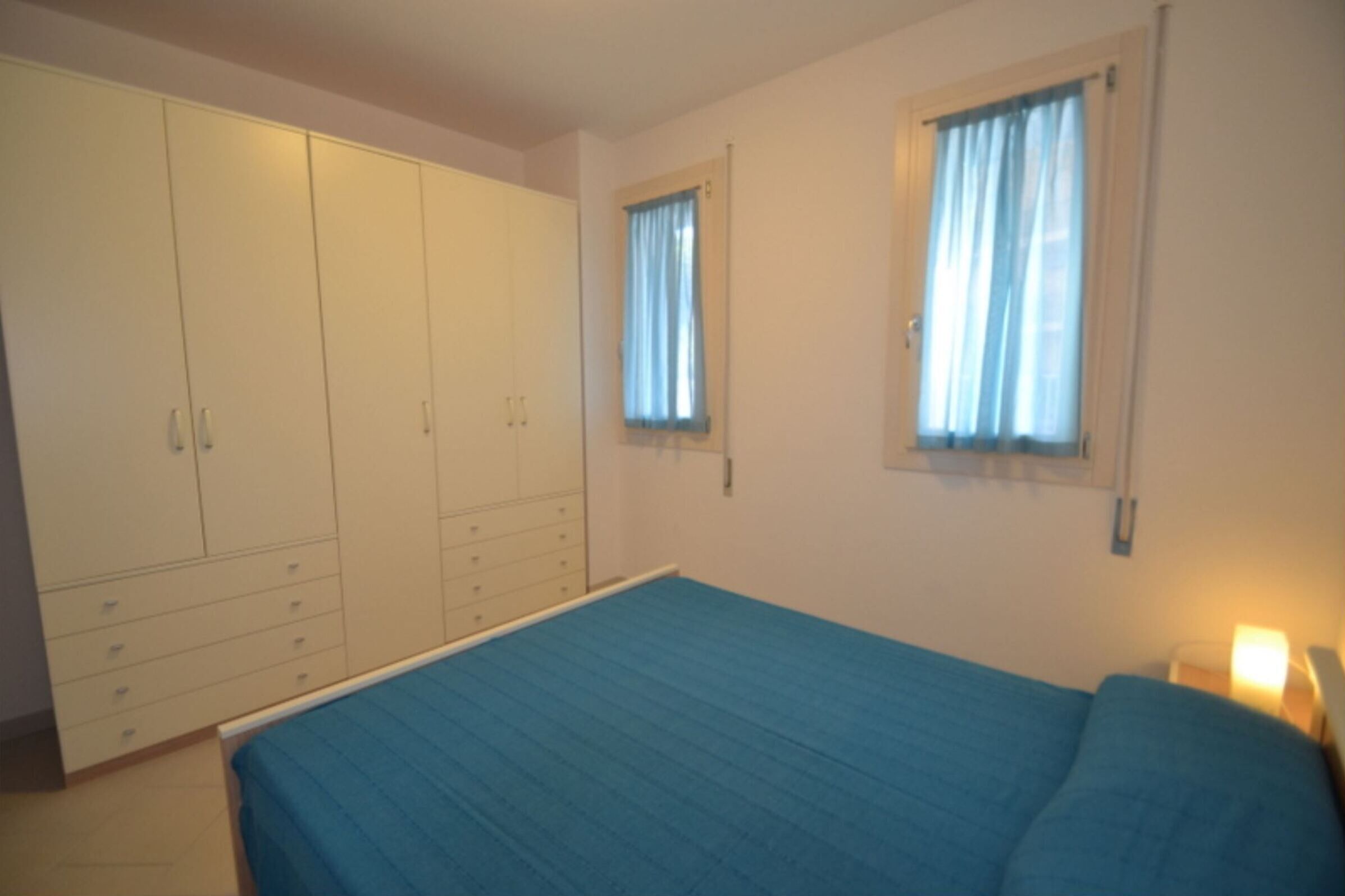 Ein Schlafzimmer mit einem Bett, einem Kleiderschrank und zwei Vorhängen an den Fenstern.