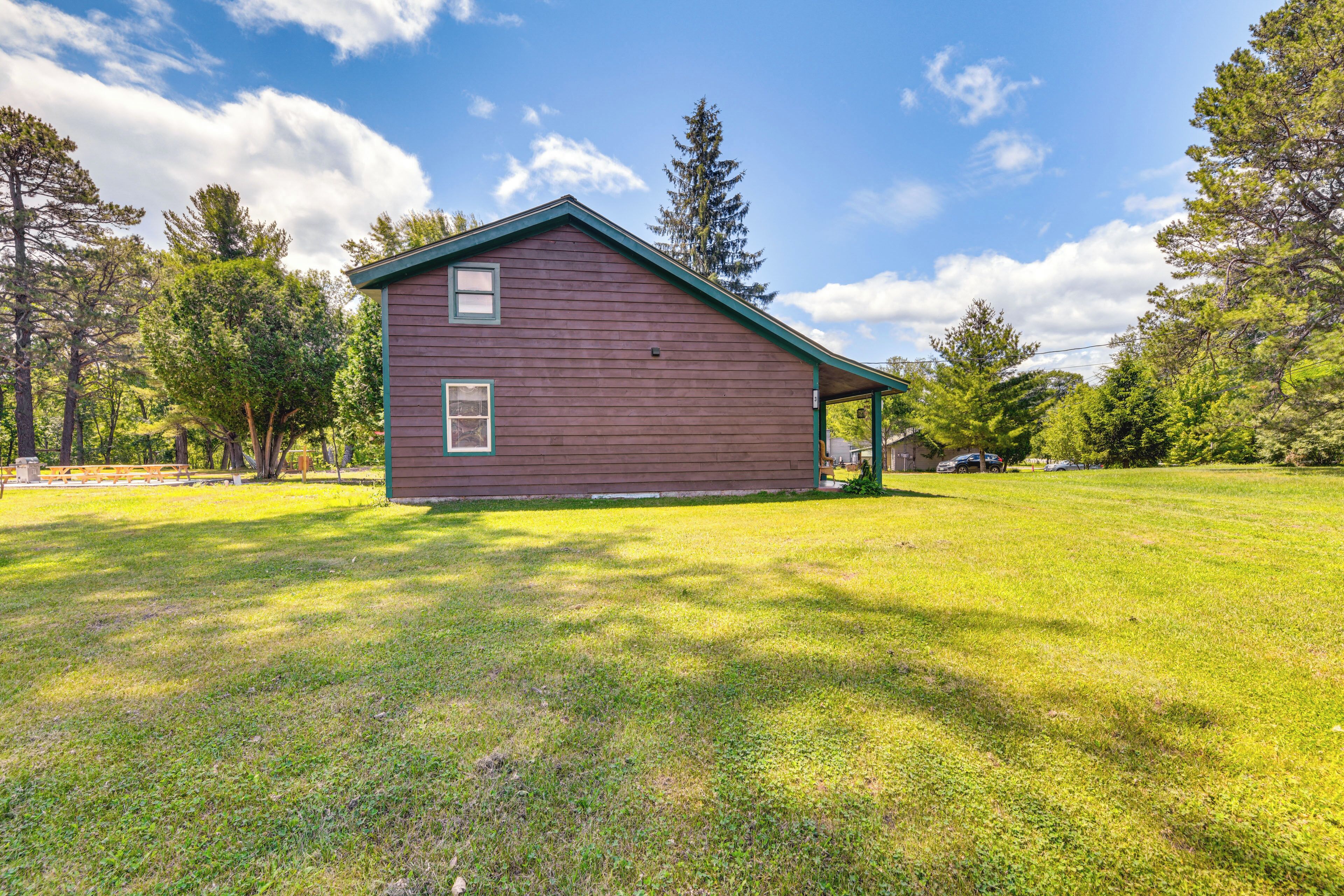 A single-story wooden house with a green roof, surrounded by a grassy yard and trees.