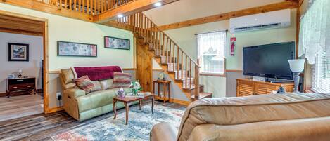 A spacious living room with a wooden staircase, a leather sofa, a coffee table, and a flat-screen TV.