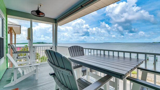 A covered outdoor deck with a table and chairs, overlooking a body of water. - Steps to Beach: Waterfront Cedar Key Home! (Cedar Key)
