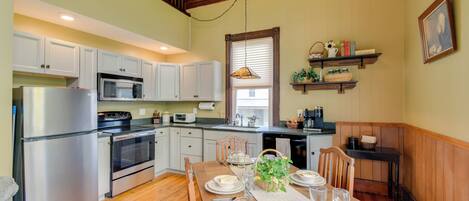 A kitchen with wooden cabinets, a stainless steel refrigerator, a microwave, and a dining table set for four.