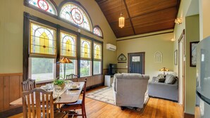 A dining area with wooden chairs, a table set for two, and large stained glass windows. - Restored Ovid Church Near Cayuga Lake Wine Trail (Ovid)