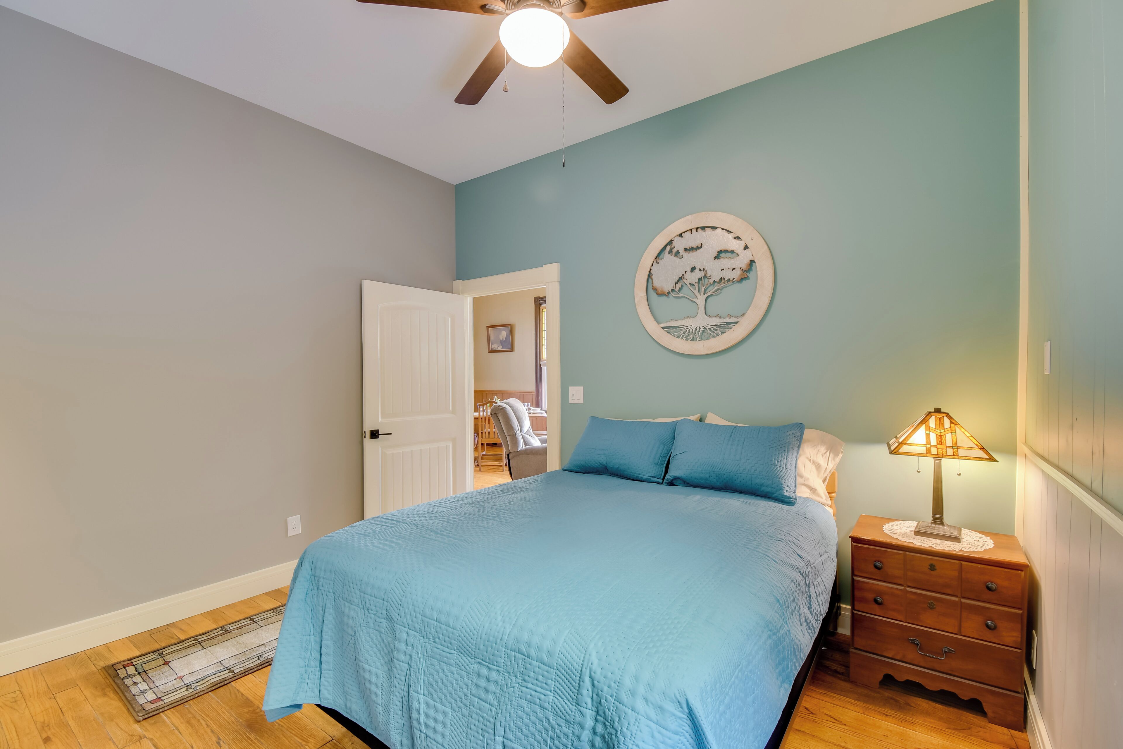 Un dormitorio con cama, mesita de noche, reloj de pared y ventilador de techo.