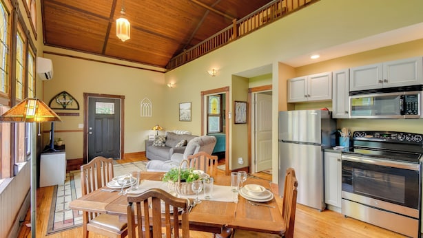 A cozy kitchen with wooden cabinets, a stainless steel oven, and a dining area with a wooden table and chairs. - Restored Ovid Church Near Cayuga Lake Wine Trail (Ovid)