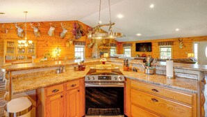 Una cucina con mobili in legno, ripiani in granito, un piano cottura in acciaio inossidabile e un lampadario.