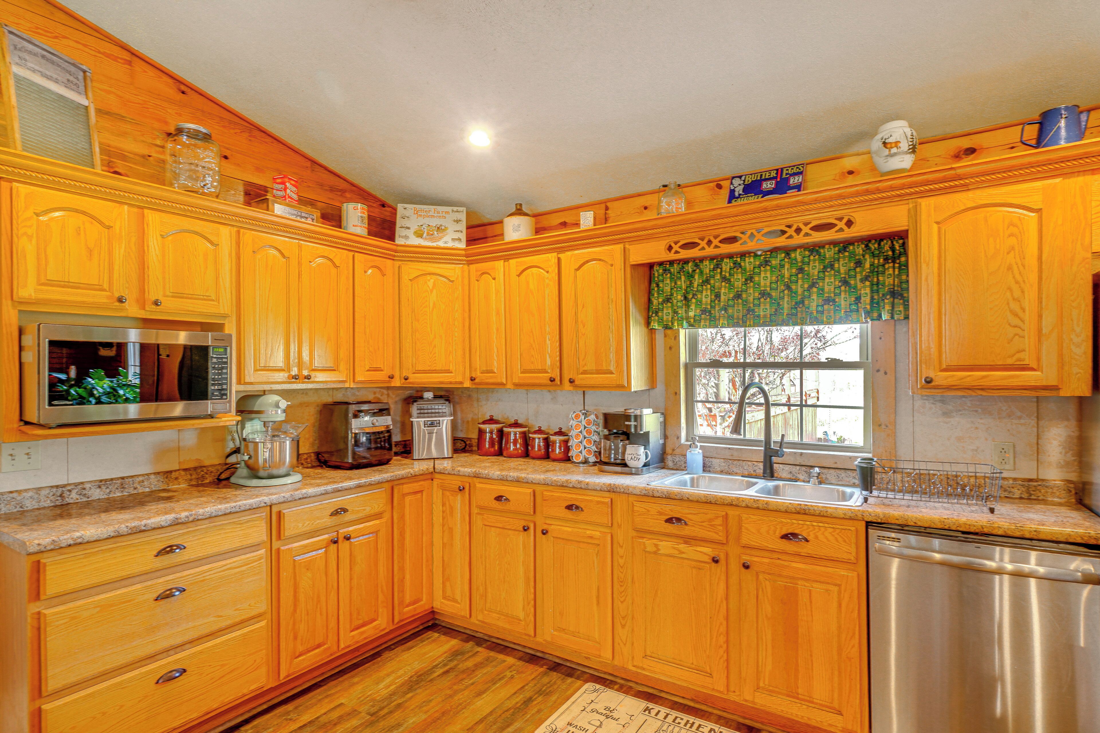 A kitchen with wooden cabinets, a stainless steel refrigerator, a coffee maker, and a window with a view of trees.