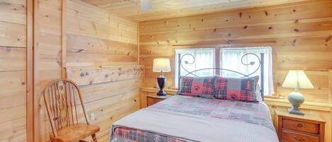 A wooden cabin bedroom with a bed, two nightstands, a chair, and a ceiling fan.