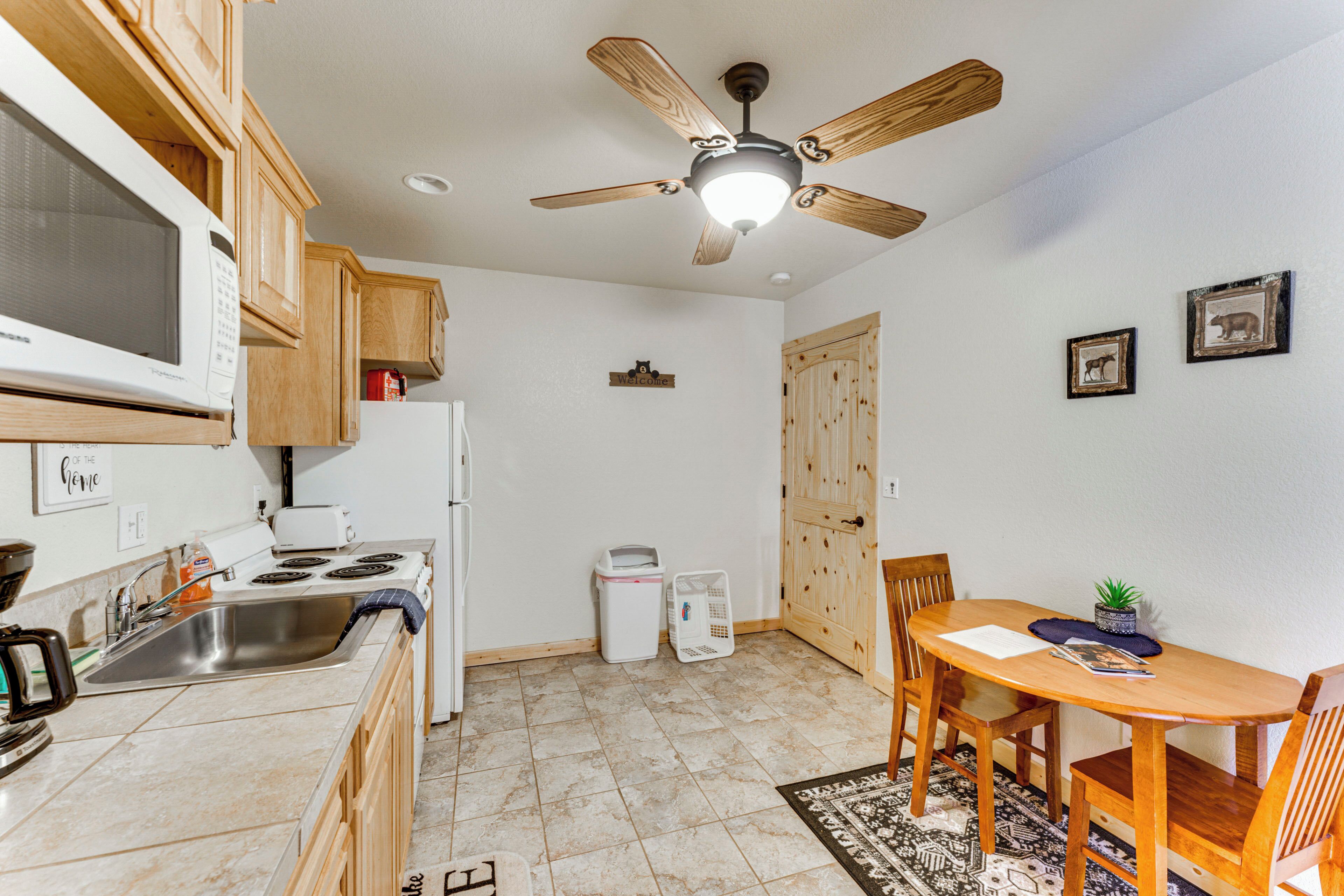 A compact kitchen with wooden cabinets, a microwave, a stove, and a ceiling fan.