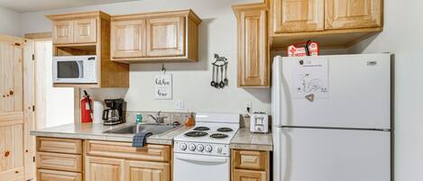 A kitchen with wooden cabinets, a microwave, a stove, a refrigerator, and a coffee maker.