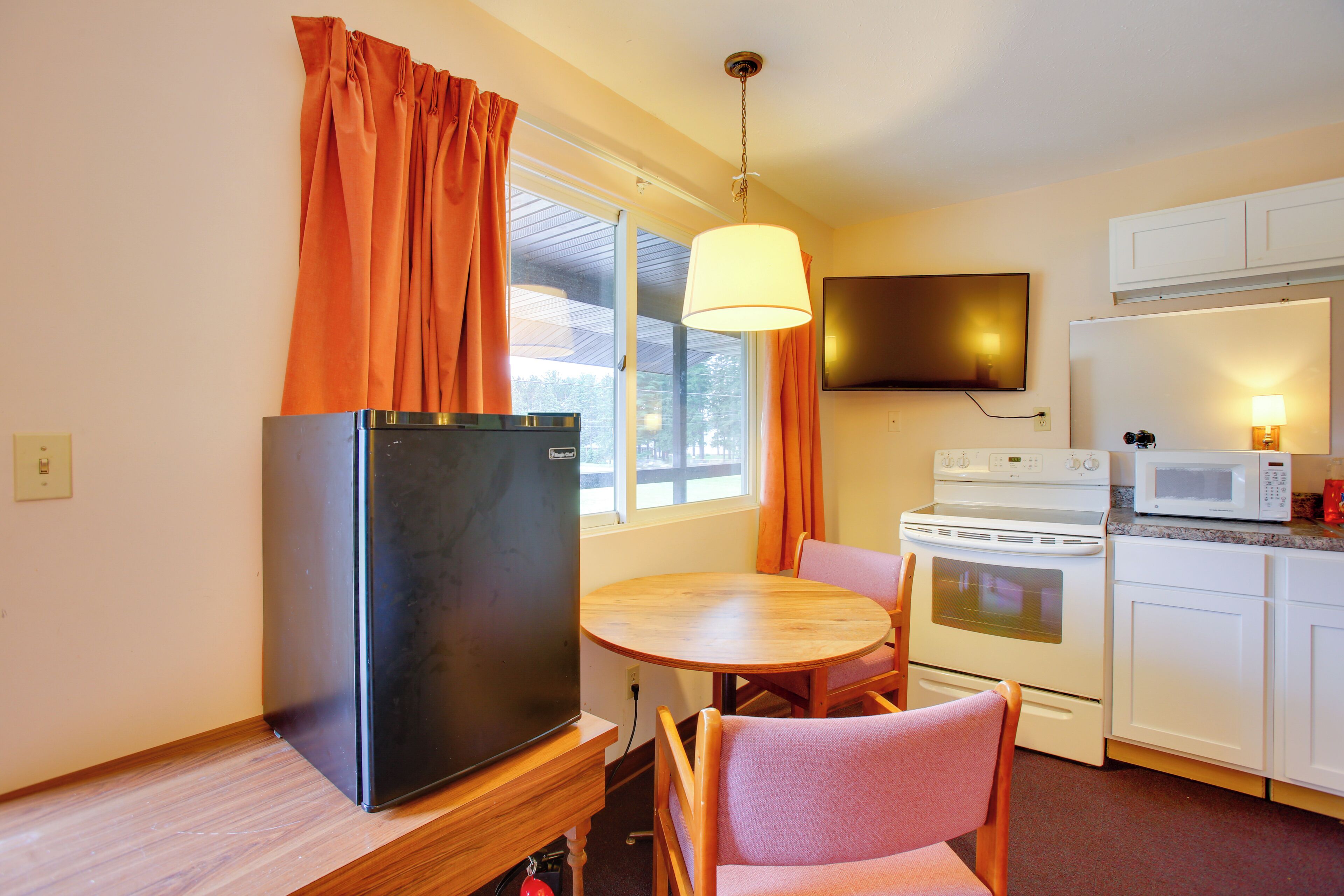A compact kitchen with a refrigerator, stove, microwave, and a dining table with chairs.