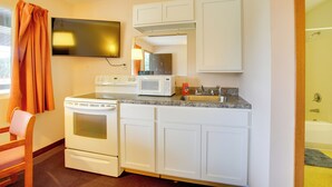 Cocina compacta con armarios blancos, microondas, estufa y lavamanos.