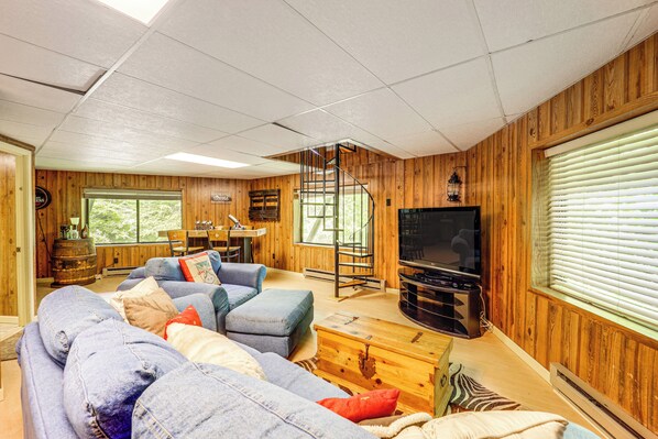 Un salon chaleureux avec un grand canapé d’angle, un meuble de rangement en bois pour les appareils multimédias et un escalier en colimaçon.