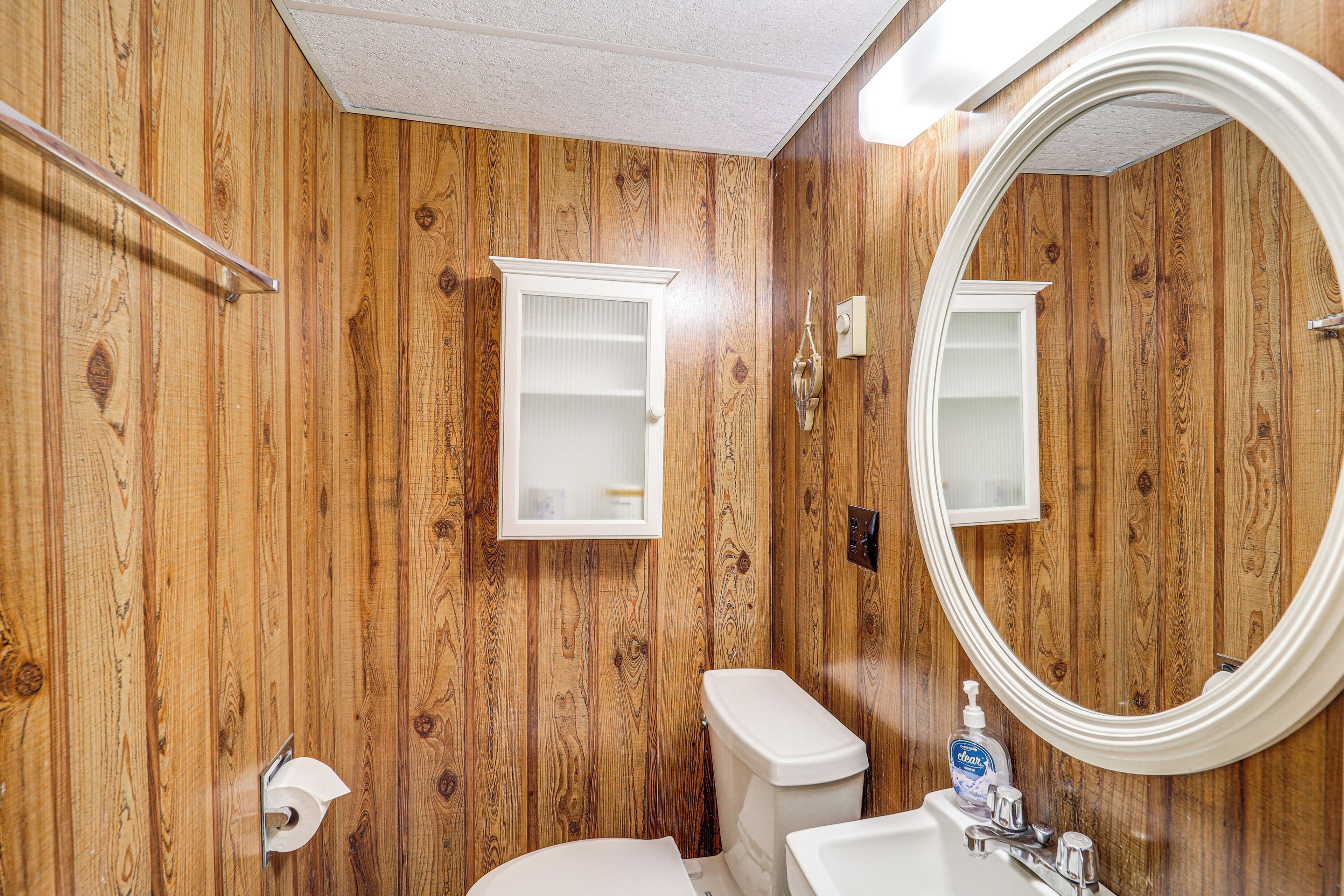 Une salle de bain aux murs lambrissés, équipée de toilettes, d’un lavabo et d’un miroir.
