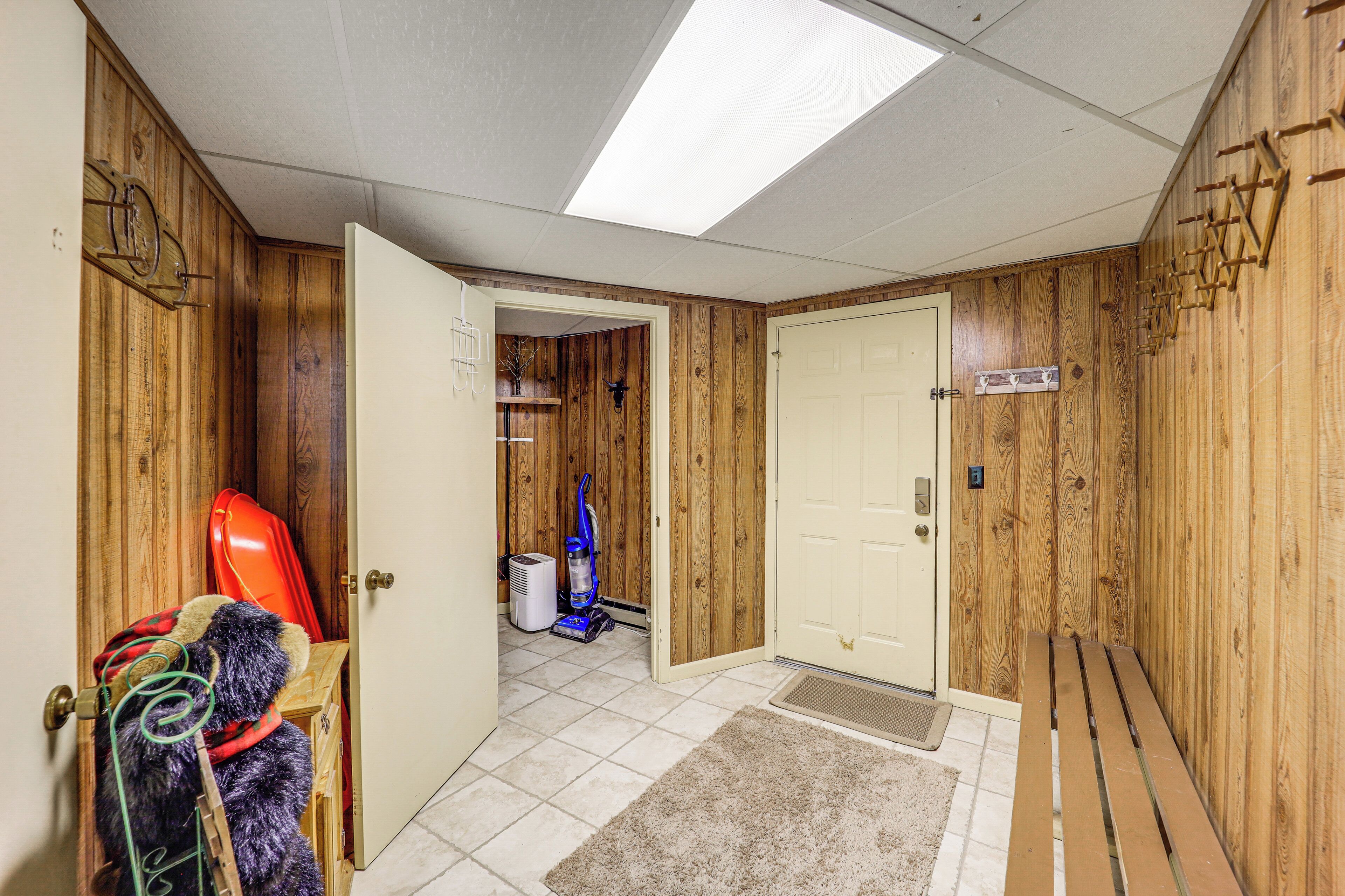 Un couloir aux murs en bois, une porte, un banc, un aspirateur et une chaise rouge.