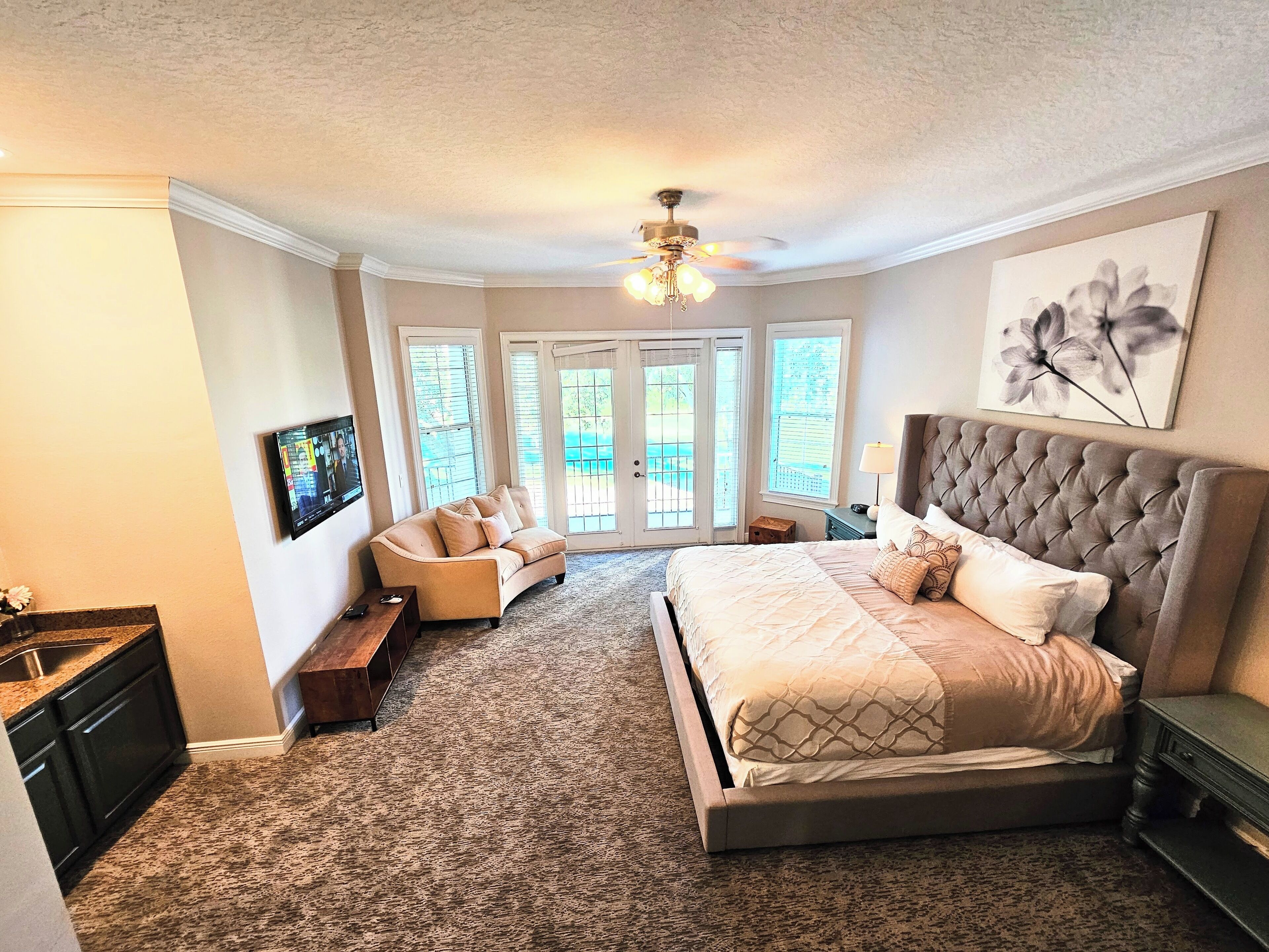 A bedroom with a large bed, a sofa, a TV, and a ceiling fan.