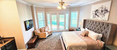 A bedroom with a large bed, a sofa, a TV, and a ceiling fan.