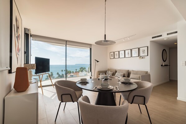 Un espace de restauration moderne doté d’une grande fenêtre, d’une table ronde dressée pour le repas et offrant une vue sur l’océan.