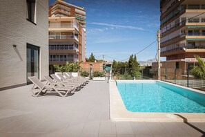 Une piscine sur le toit, agrémentée de chaises longues, entourée d’immeubles à plusieurs étages dotés de balcons.