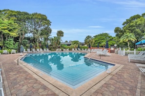 A rectangular swimming pool with a tiled deck surrounding it, equipped with lounge chairs and umbrellas. - I-353 - Designer Furnished and Views & Sleeps 6 (Naples)