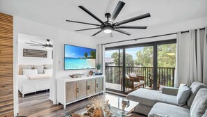 A modern living room with a glass coffee table, a sofa, a TV, and a balcony with outdoor furniture.