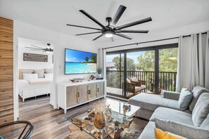 A modern living room with a glass coffee table, a sofa, a TV, and a balcony with outdoor furniture. - I-353 - Designer Furnished and Views & Sleeps 6 (Naples)