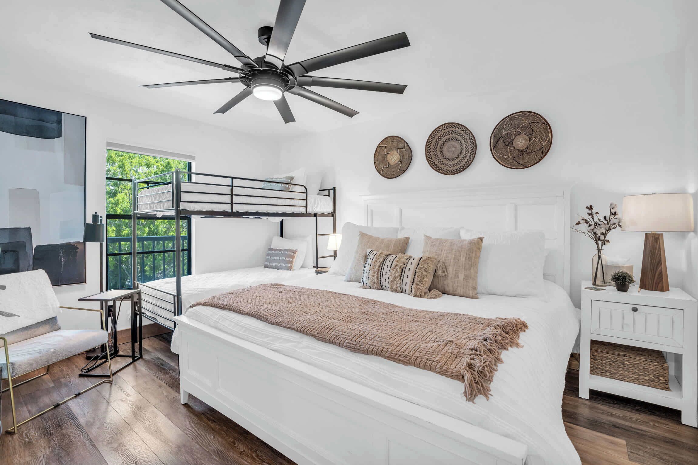 Een moderne slaapkamer met een groot bed, een plafondventilator en uitzicht op groen.