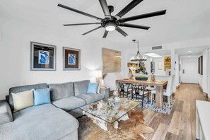 A modern living room with a gray sectional sofa, a glass coffee table, and a ceiling fan.
