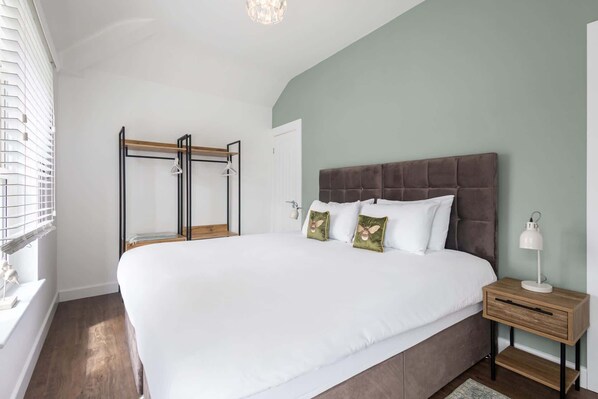 A bedroom with a large bed, a nightstand, a wooden bench, and a window with blinds.
