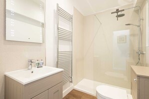Ein modernes Badezimmer mit einer Glaskabine zur Dusche, einem weißen Waschbecken mit Spiegel darüber und einer Toilette.