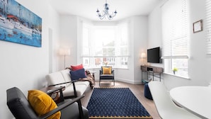 En moderne stue med sofa, stole, spisebord og fjernsyn.