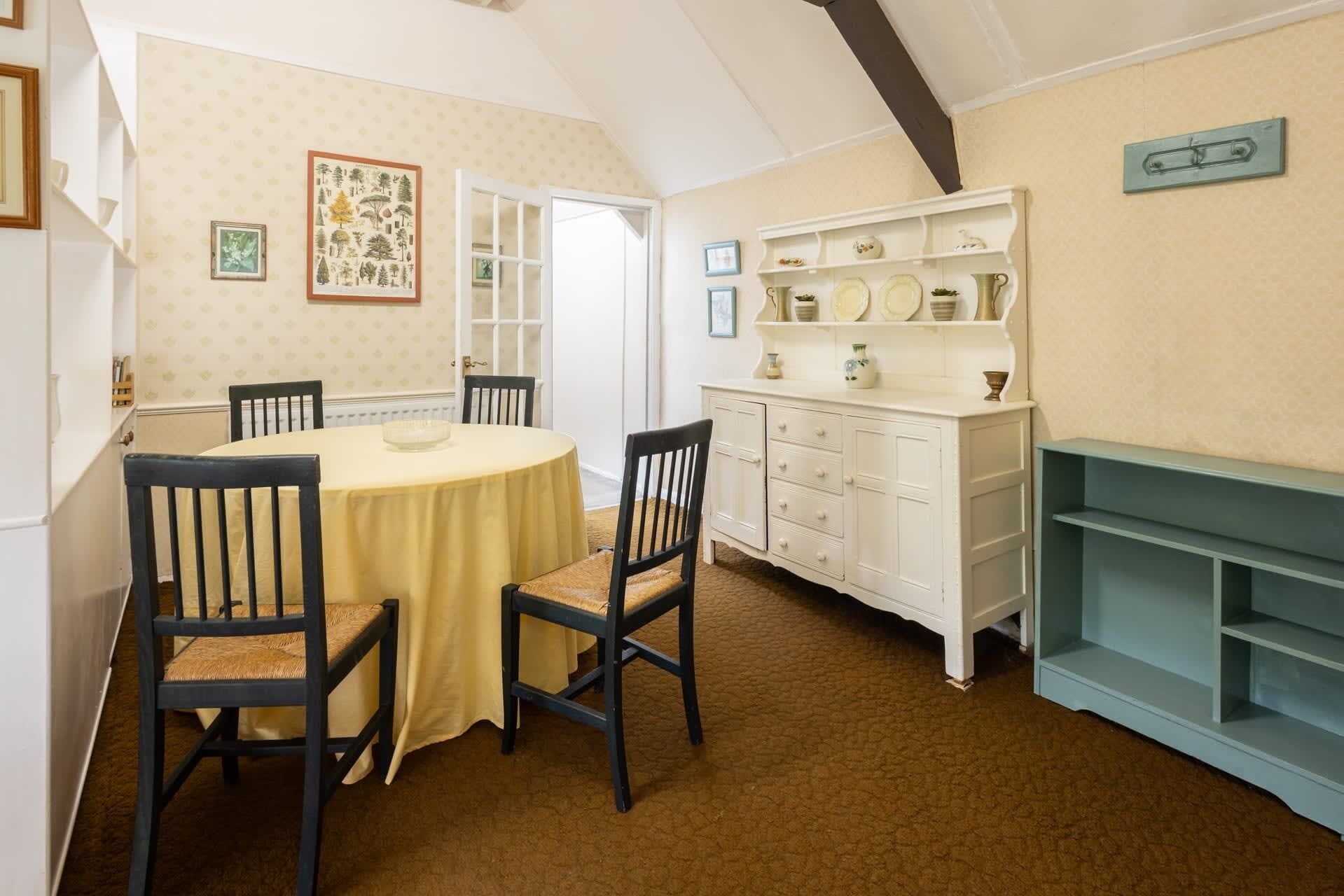 A dining room with a round table, two chairs, a white cabinet with shelves, and a door leading to another room.