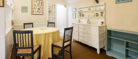 A dining room with a round table, two chairs, a white cabinet with shelves, and a door leading to another room.