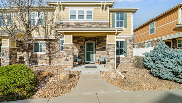 A two-story house with a stone facade, a front porch with chairs, and a well-maintained garden. - Flyer's Nest Townhome (Westminster)