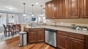 A modern kitchen with wooden cabinets, a dishwasher, and a granite countertop. - Flyer's Nest Townhome (Westminster)