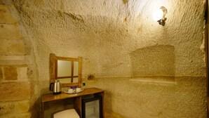 Una stanza piccola e rustica con una parete in pietra, un tavolo di legno con un bollitore, un piccolo frigorifero e uno specchio.
