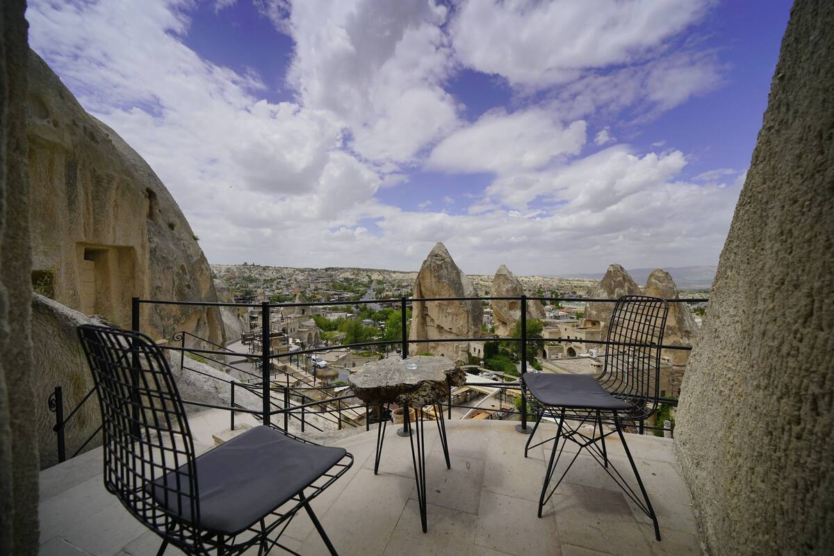 Una terraza al aire libre con dos sillas de metal negro y una mesa pequeña, con vistas a un paisaje urbano con formaciones rocosas distintivas.