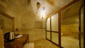 Un bagno con pareti in pietra, una panca in legno, un bollitore e una tazza sul lavabo.