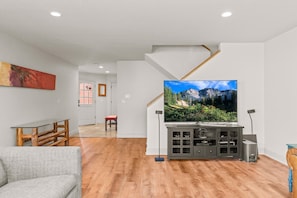 Ein modernes Wohnzimmer mit einem großen Flachbildfernseher, Holzböden und einer Treppe, die eine weitere Ebene hinaufführt.