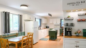 A compact kitchen with white cabinets, a dining table with chairs, a coffee machine, and a tea station.