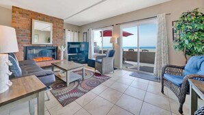 Un salón espacioso con chimenea, televisor y balcón con vistas al océano.