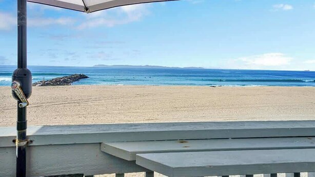 Vista de la playa con un paraguas a rayas y un banco de madera.