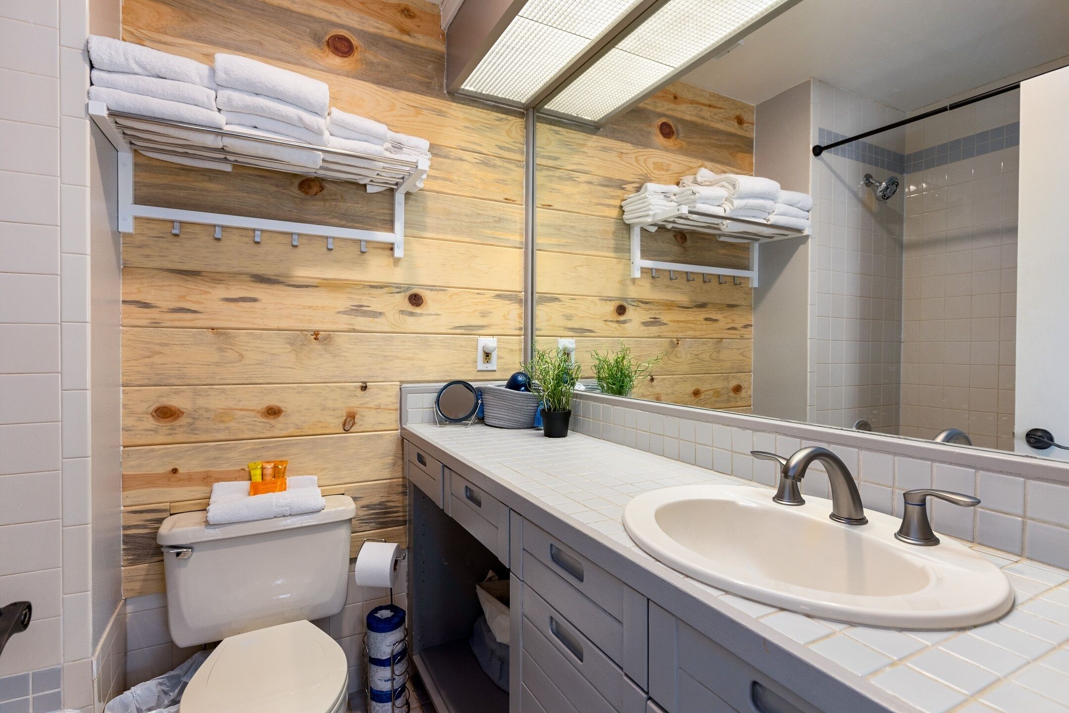 Un baño moderno con pared de madera, un espejo grande, un lavamanos y una ducha.