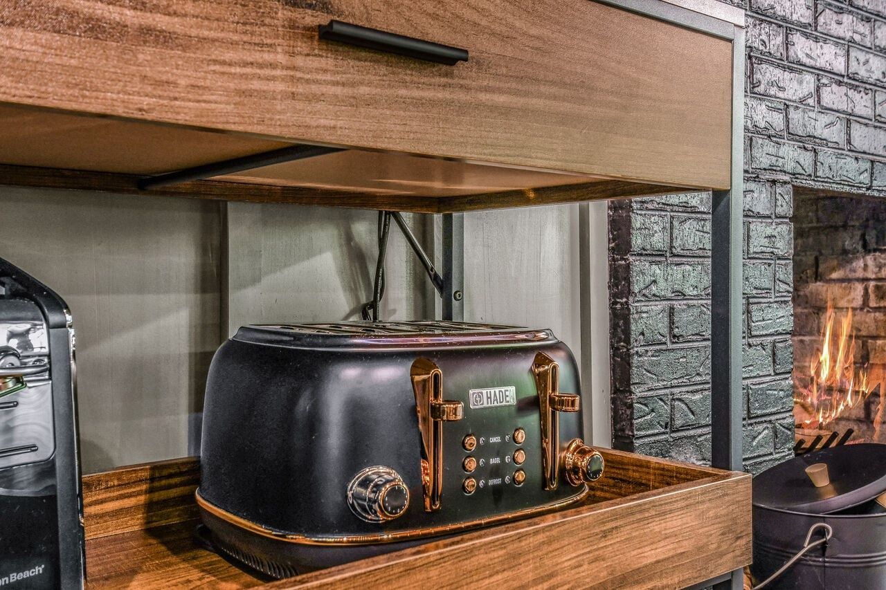 A vintage-style toaster on a wooden tray in a kitchen with a brick wall and a fireplace.
