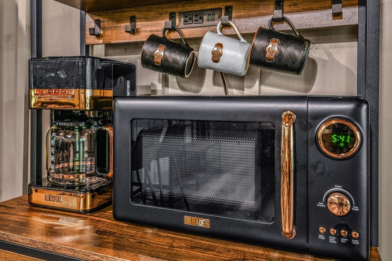 A black microwave with a digital clock and a coffee maker on a wooden surface.