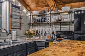 A kitchen with a black stove, wooden shelves, and a granite countertop. - Light'n Bug Bungalow 1 Bedroom Cabin by RedAwning (Townsend)