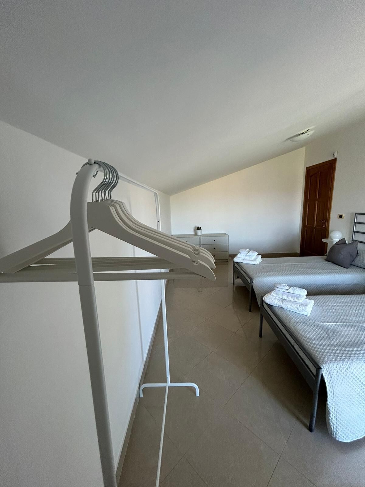 Ein Hotelzimmer mit zwei Betten, einem weißen Kleiderhaken, einem kleinen Tisch mit Lampe und einer Tür im Hintergrund.